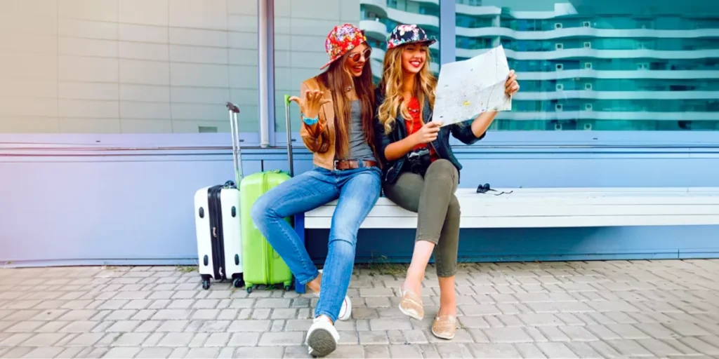 Dos-chicas-alegres-mirando-en-el-mapa-con-sus-maletas