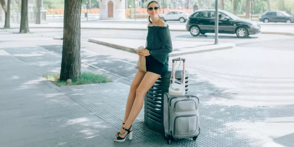 Mujer-con-gafas-de-sol-sentada-en-su-maleta-de-mano-pequena