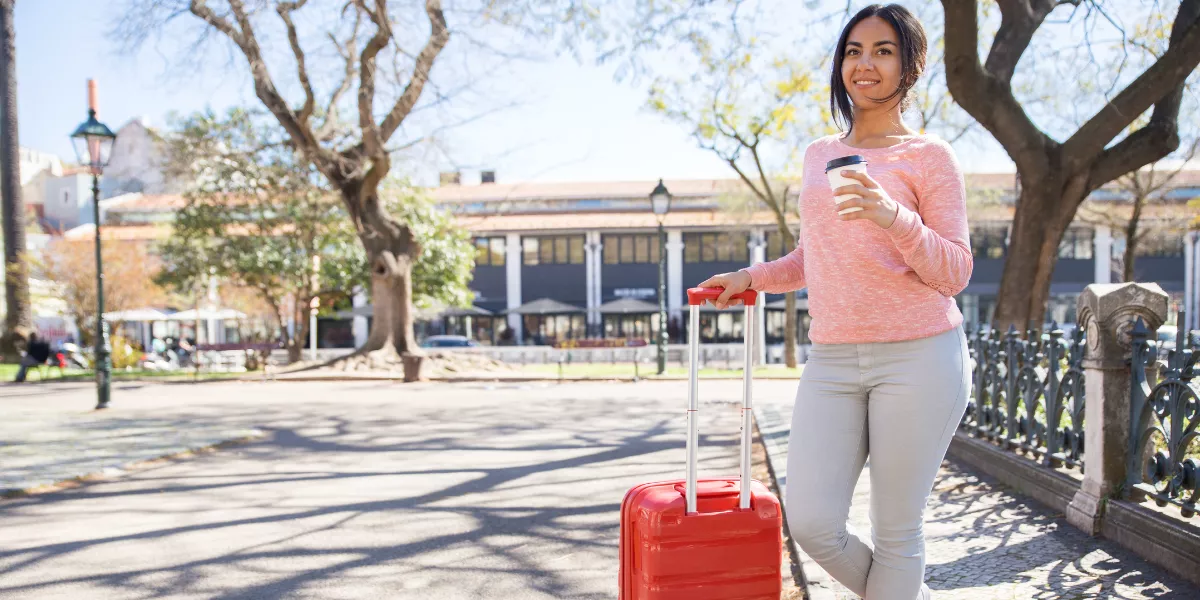 Mujer-con-su-maleta-pequena-toma-su-cafe-al-aire-libre